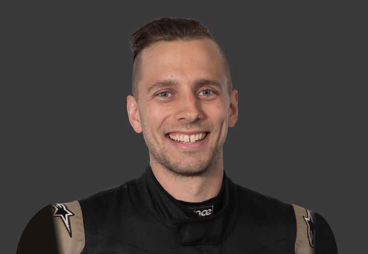 A headshot of professional T G R A driver Luke King in a black and taupe racing suit against a grey background.