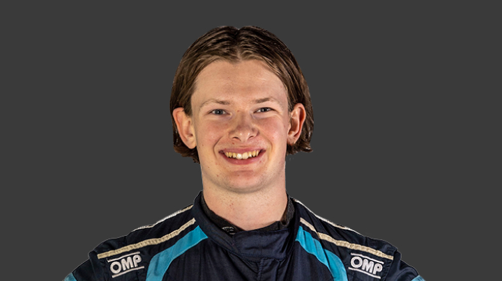 A headshot of professional T G R A driver Campbell Logan in a navy, blue and white racing suit on a grey background.