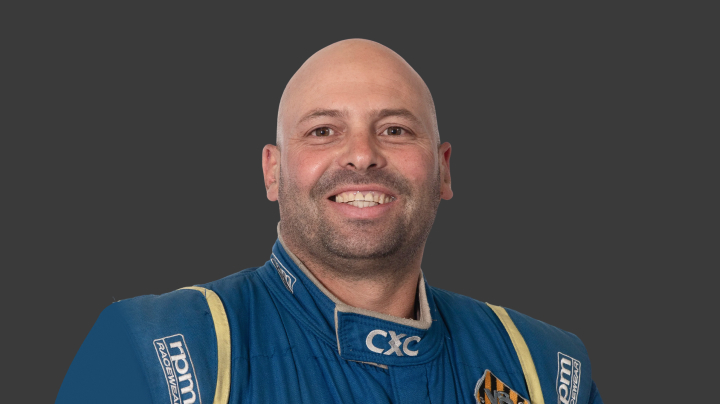 A headshot of professional T G R A driver Dylan Thomas in a blue and yellow racing suit on a grey background.