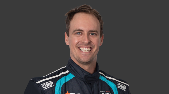 A headshot of professional T G R A driver Tim Brook in a navy, blue and white racing suit background.