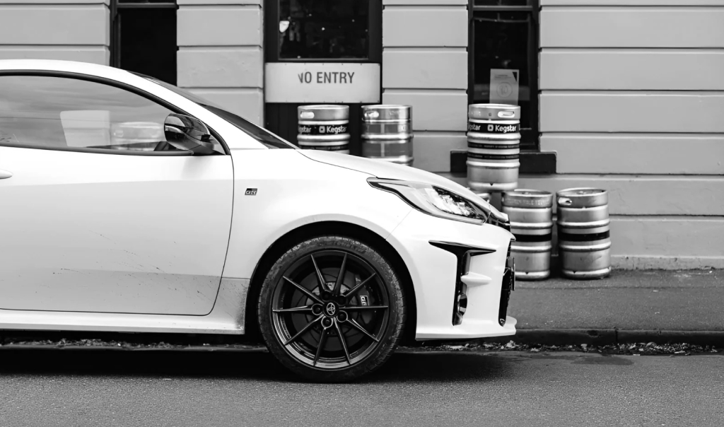 A Glacier White Toyota G R Yaris parked in front of The Rose Hotel, Fitzroy, with beer kegs stacked on the footpath against the beige facade.