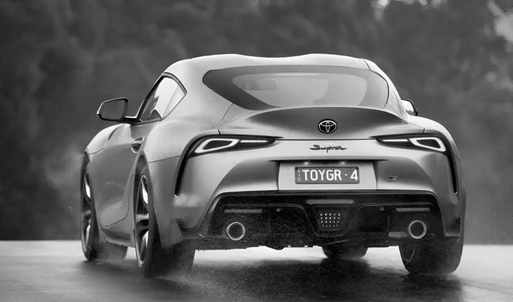 A G R Supra in Nurburg Matte Grey driving along a wet road, Australian bushland visible in the distance ahead.