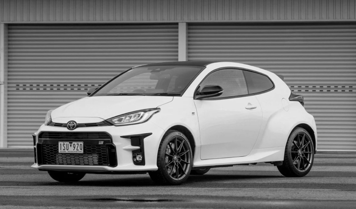 A G R Yaris in Glacier White parked on a wet test track in front of a pair of grey corrugated warehouse doors.