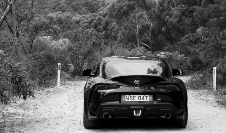 A G R Supra in Bathurst Black, driving down an unsealed road in the bush towards the Blue Mountains.