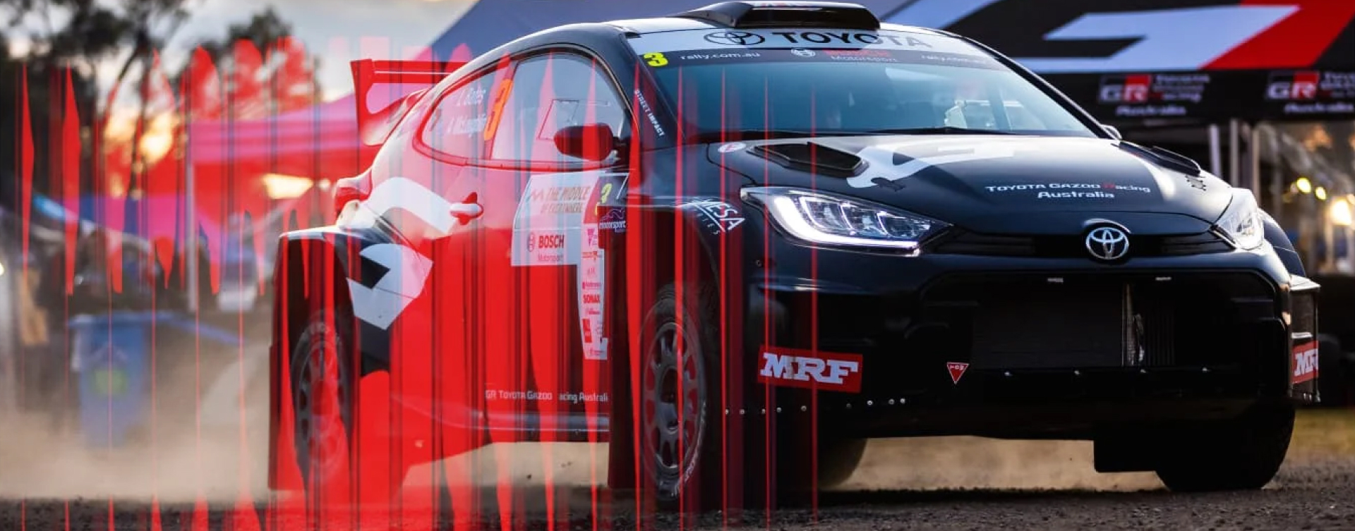 A Toyota GR Yaris Rally2 in Tarmac Black in racing livery. T G R stalls sit in the background. A red '2' with a corrugated glass texture is superimposed.