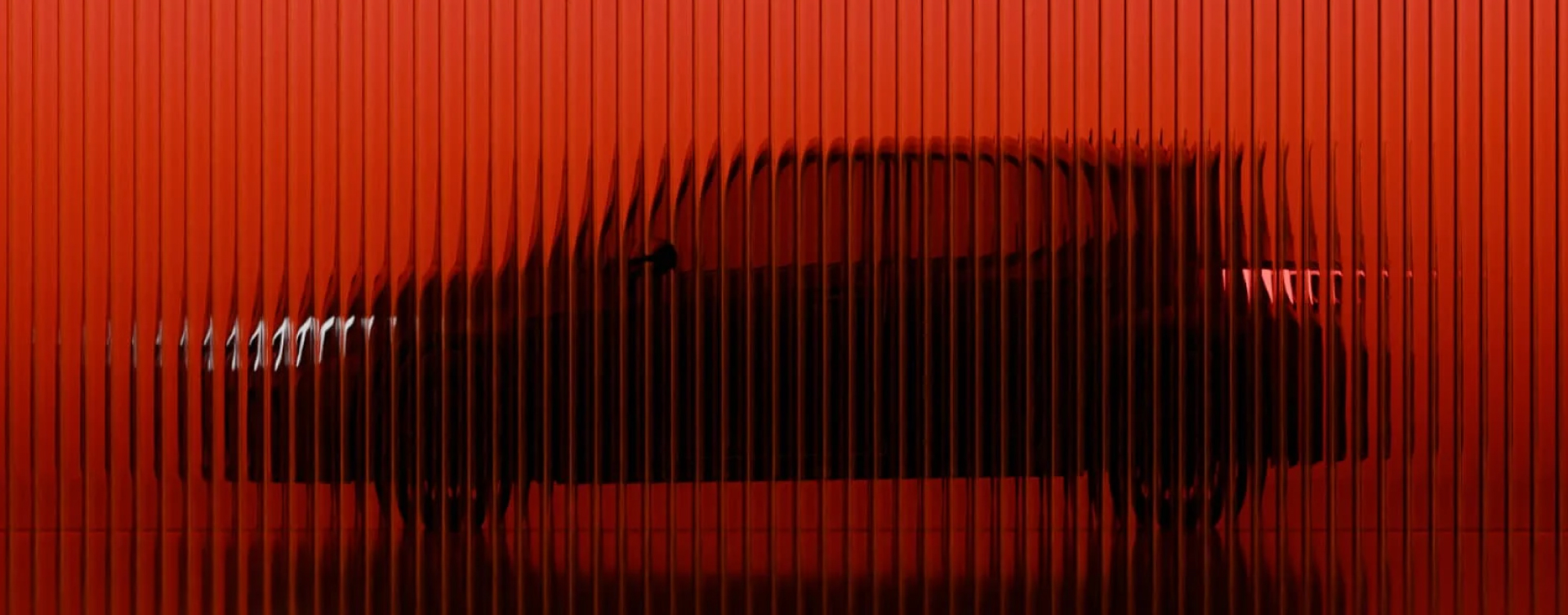 The right-side profile of a Toyota G R Yaris in an orange studio. The vehicle sits behind a pane of corrugated glass, warping the vehicle for an artistic effect.
