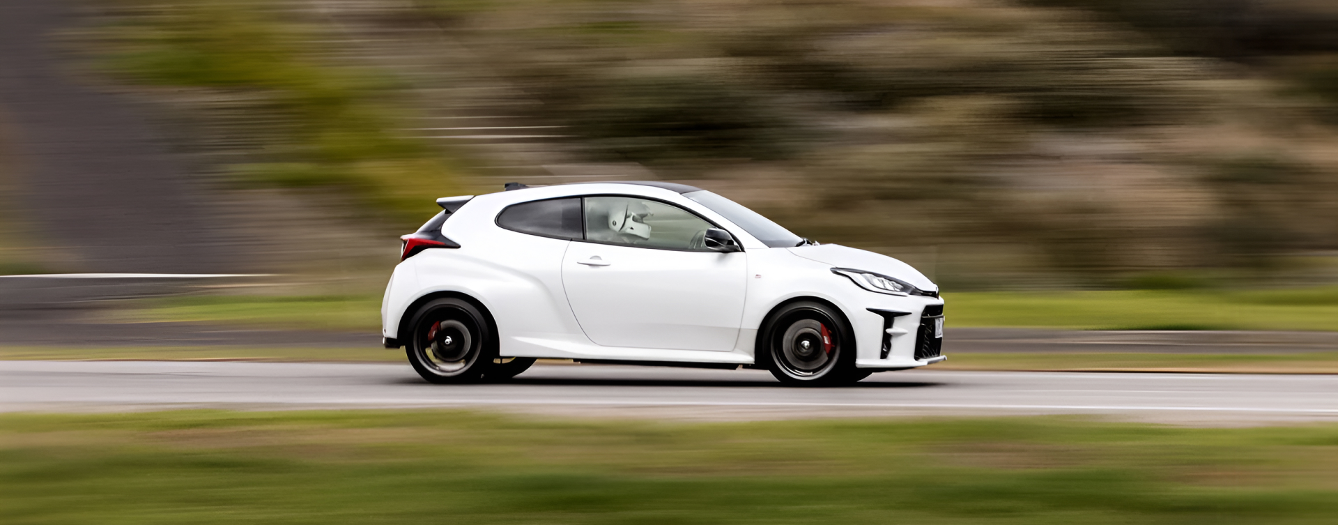 A Toyota G R Yaris in Glacier White racing around a track. The vehicle is in focus, its surroundings a blur as it moves at speed.