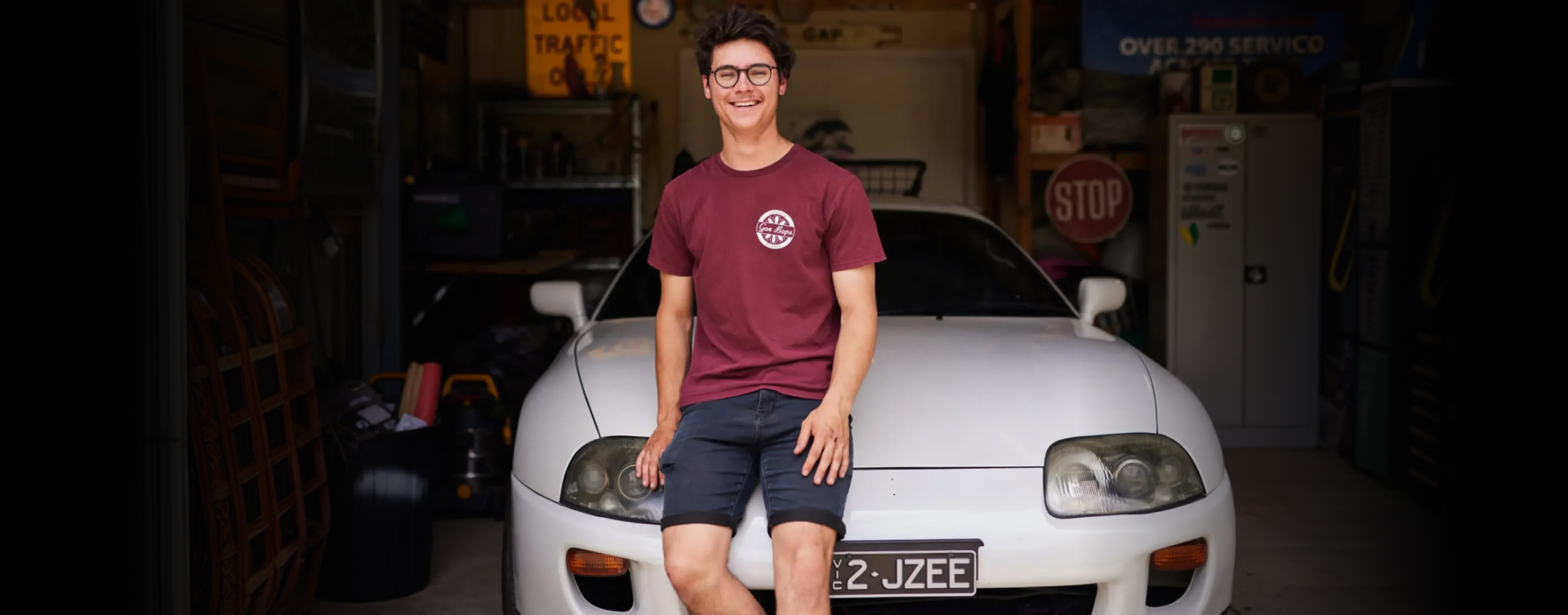 Toyota owner Anthony Roperto sits against the bonnet of his white M k 4 Supra in his home garage, smiling.
