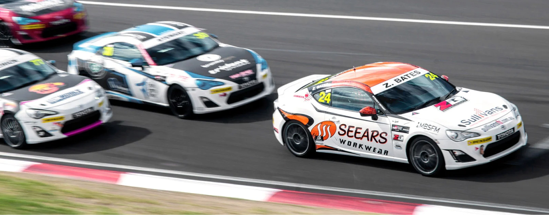 Four Toyota G R 86 vehicles in racing livery competing for first place. The frontrunner is in clear focus, while the other three competitors are blurred from the speed at which they're racing.