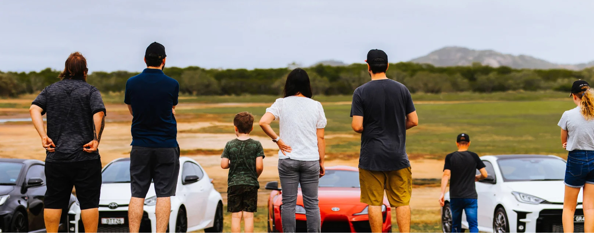 Gazoo Racing Club members from Townsville stand side by side, admiring their Toyota G R vehicles parked overlooking an open plain in rural Queensland.