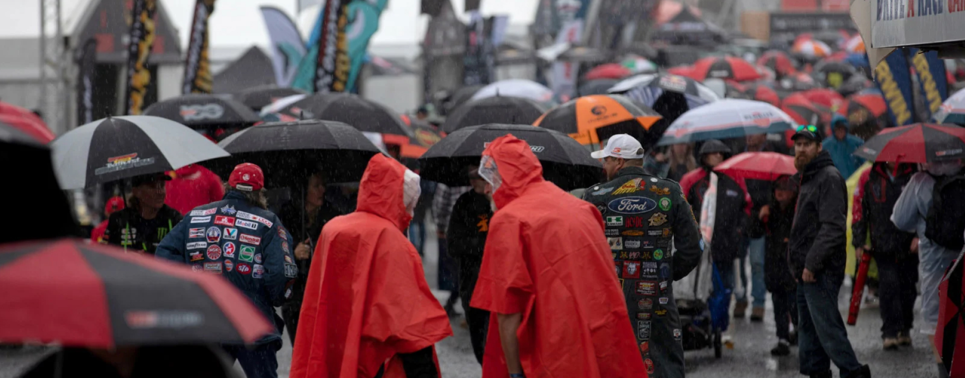 Crowds of people under raincoats and umbrellas flocking toward the entry of the Bathurst 1000 under heavy rain.