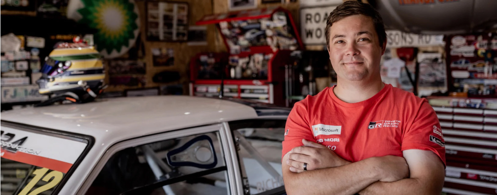 Toyota owner Ayrton Richardson, smiling, arms crossed in his home garage, wearing a T G R A shirt.