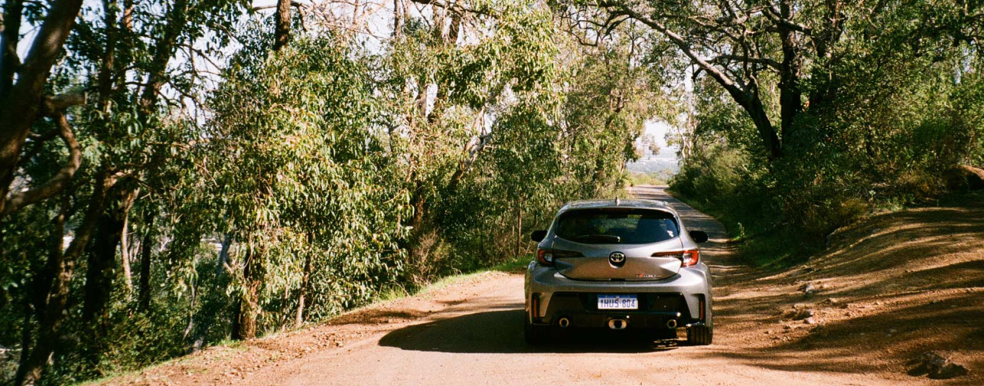 A Toyota G R Corolla in Liquid Mercury, driving down a road in the Western Australian bush.