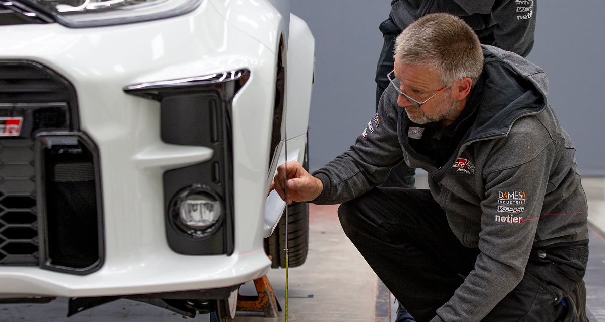 A technician measuring the wheel clearance on a white Toyota G R Yaris.