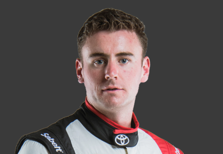 A headshot of professional T G R A driver Harry Bates in a white, black and red racing suit. Grey background.