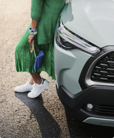 Woman in a green skirt and cardigan leans against a silver Toyota RAV4.