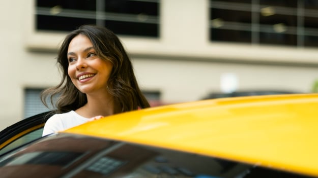 A smiling woman exits a yellow passenger car.