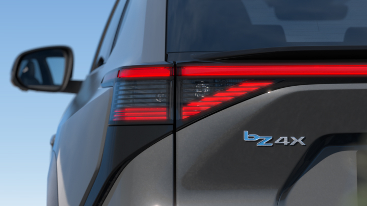 A rear view of the all-electric Toyota bZ4X in the liquid metal paint colour, with red tail lights and a bZ4X badge. 