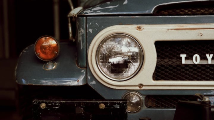 The close-up of a worn and tattered LandCruiser headlight.