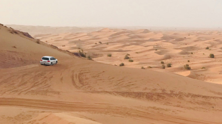 A white LandCruiser driving along hilly desert dunes.