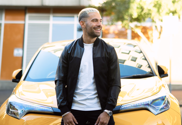 A man smiles as he leans on the front of a yellow Toyota C-HR.