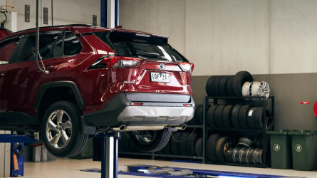 The rear view of a maroon Toyota RAV4 raised on a hoist inside a workshop next to racks holding tyres.