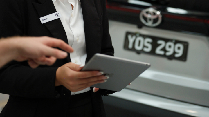 A Toyota representative holding a tablet while interacting with a customer beside a white vehicle.