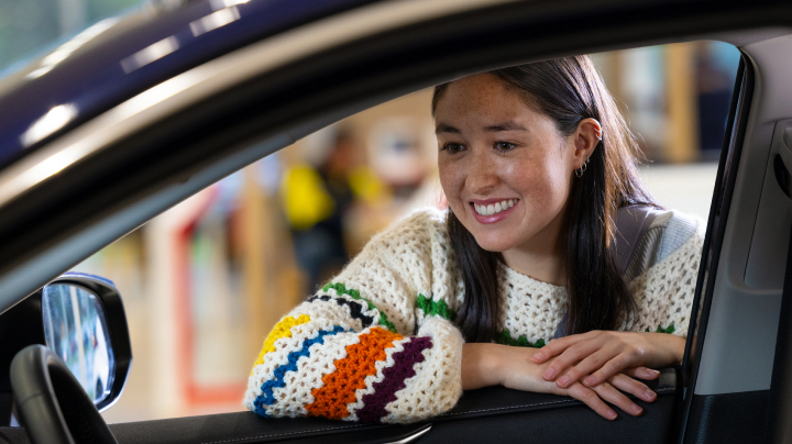 A woman smiles as she leans in the open window of a vehicle.