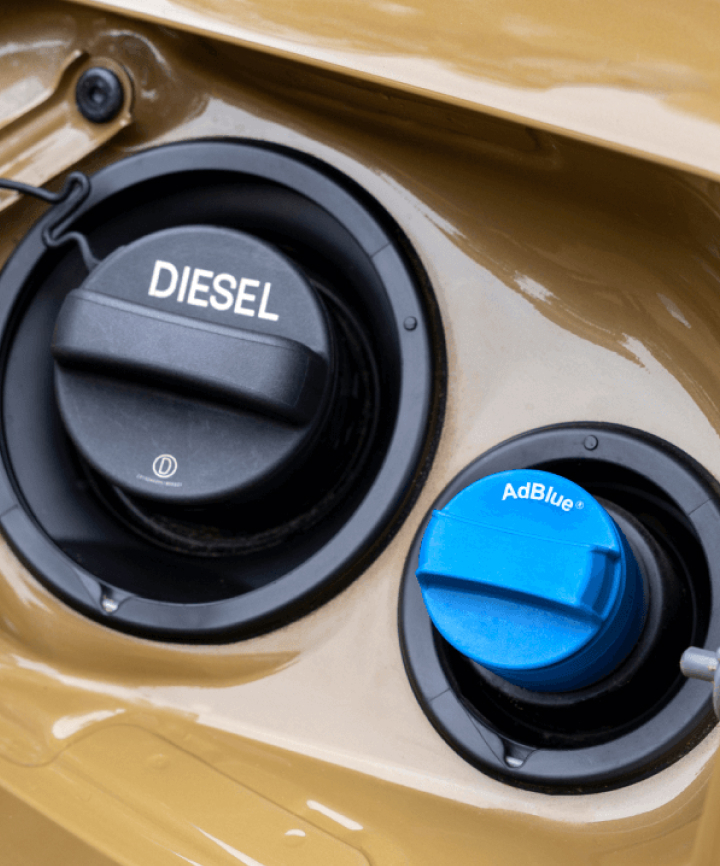 A vehicle's open fuel filler compartment, showing a black cap labelled "DIESEL" alongside a smaller blue cap labelled "AdBlue".