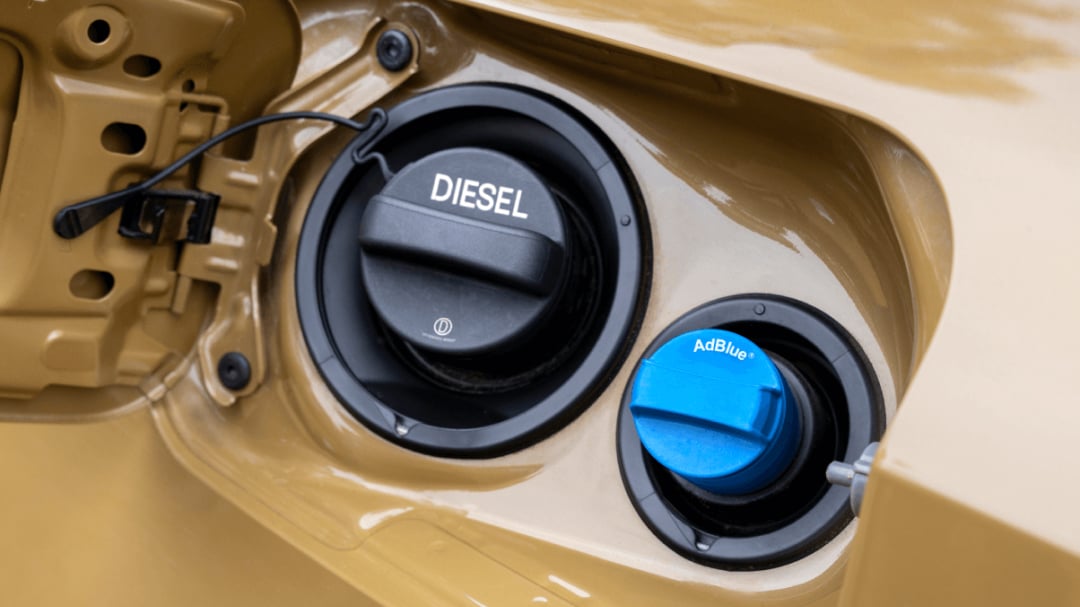 A vehicle's open fuel filler compartment, showing a black cap labelled "DIESEL" alongside a smaller blue cap labelled "AdBlue".