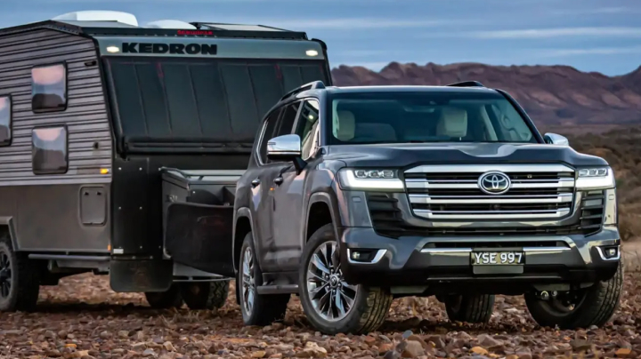 A grey Toyota LandCruiser 300 towing a Kedron caravan through a desert.