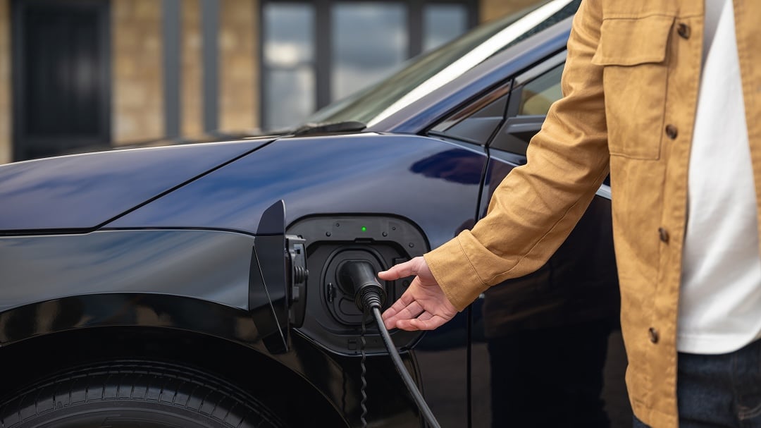 A person plugs a charging cable into the side charging port of a blue Toyota bZ4X.