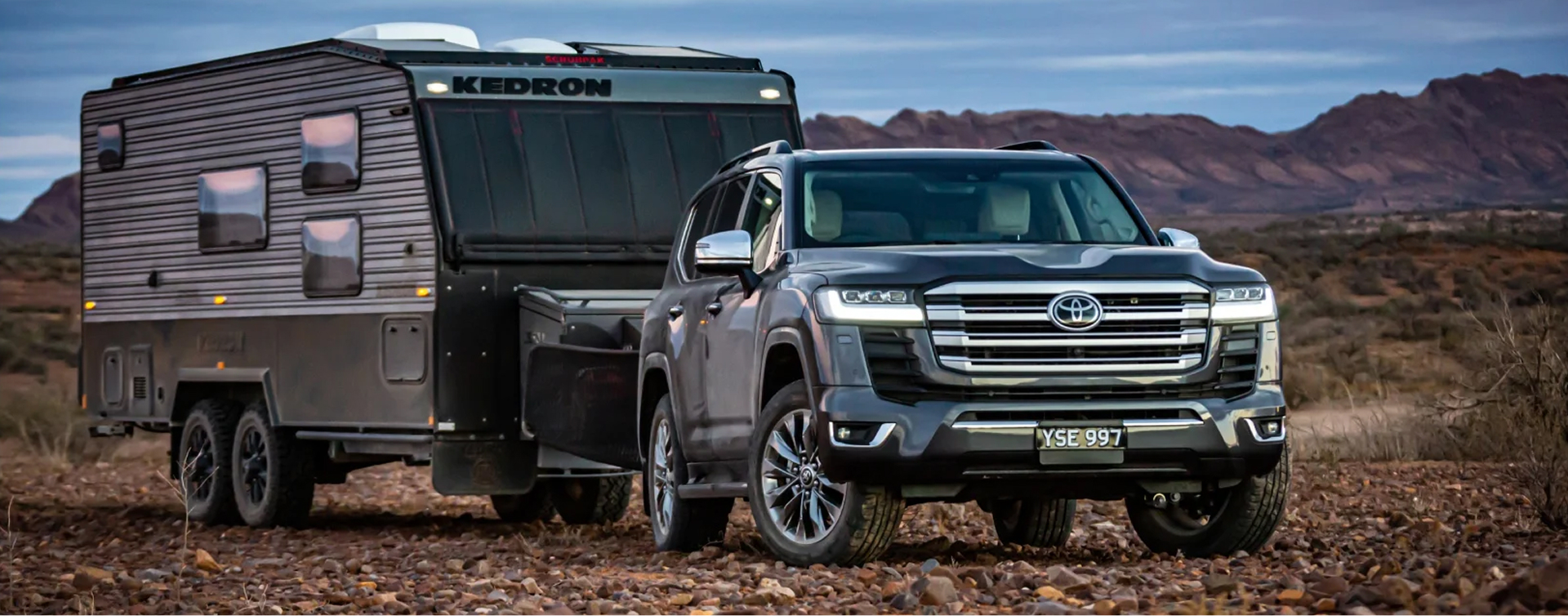 A Toyota LandCruiser 300 towing a caravan across a rocky plane in the Australian outback.
