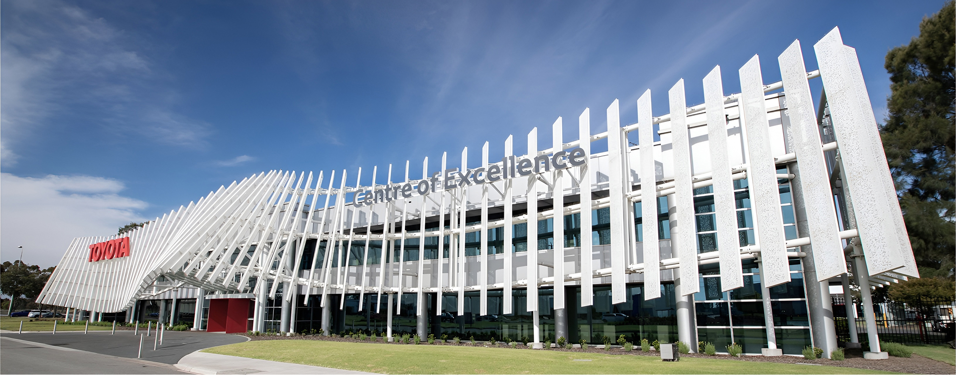 The modern exterior of Toyota's Centre for Excellence in Altona, Victoria. The unique facade is composed of a series of vertical panels that sweep across the front of the building, with a wave in the centre, where the building’s entrance is located. 