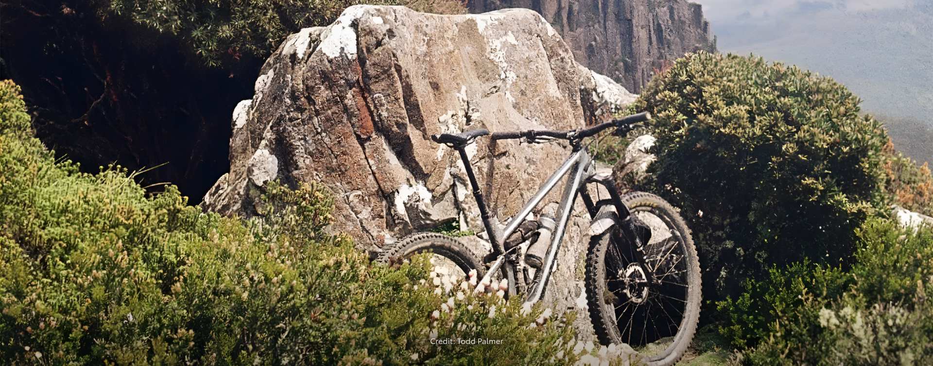 A silver mountain bike, leaning against a large rock in the mountainous Australian bush.