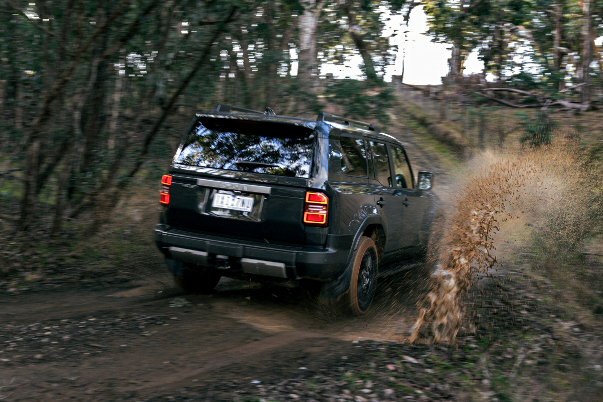 A Toyota LandCruiser Prado in Eclipse Black, driving down a dirt road in the bush, kicking up mud and water.