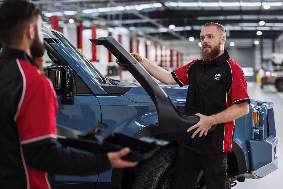 A Toyota mechanic wheels a large 4x4 tyre across the floor of a Toyota service centre.
