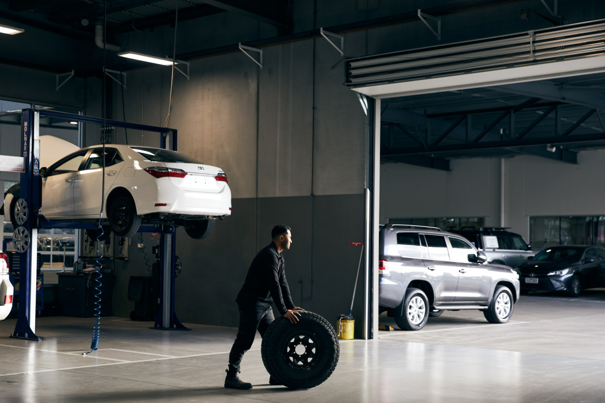 A Toyota mechanic wheels a large 4x4 tyre across the floor of a Toyota service centre.