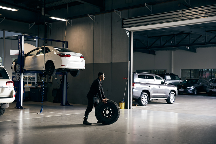 A Toyota mechanic wheels a large 4x4 tyre across the floor of a Toyota service centre.