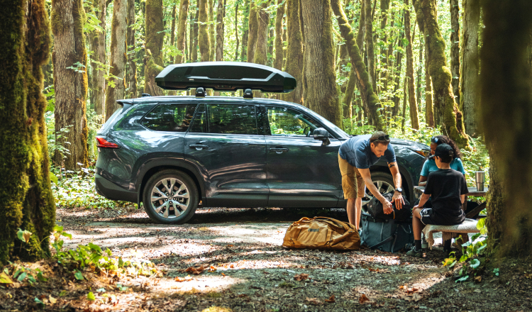 Toyota SUV equipped with Genuine Roof Racks parked at a forest campsite with a family.
