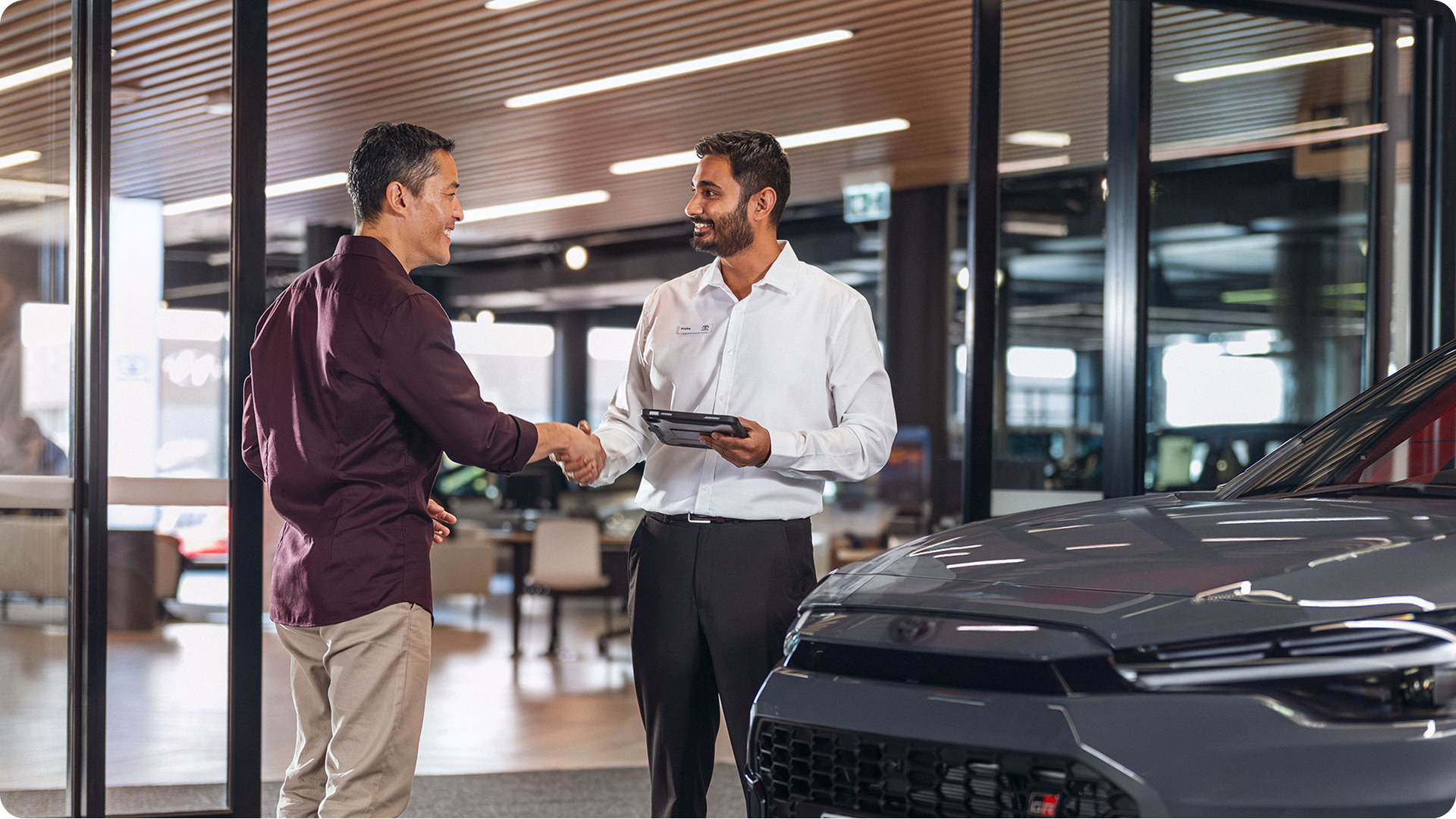 Customer shaking hands with a Toyota staff member next to a vehicle inside a showroom.