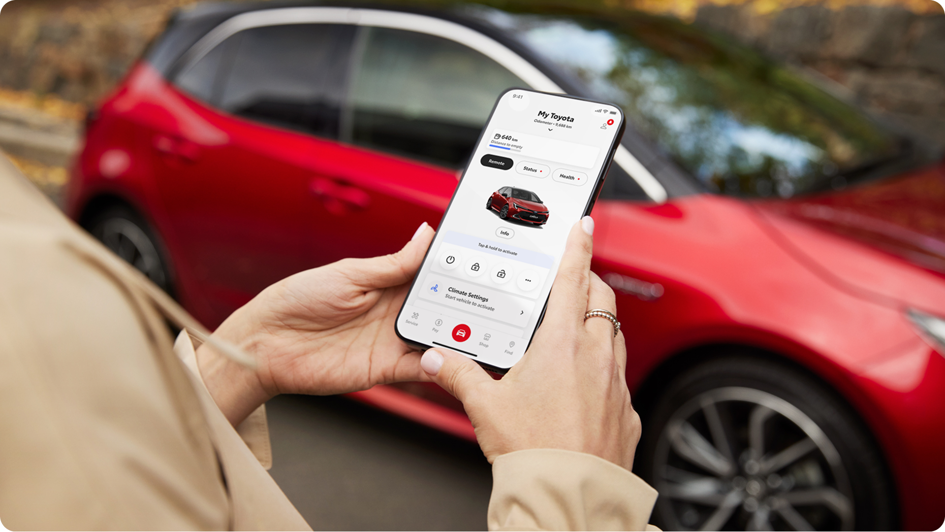Person holding a smartphone using the My Toyota connected app in front of a red vehicle