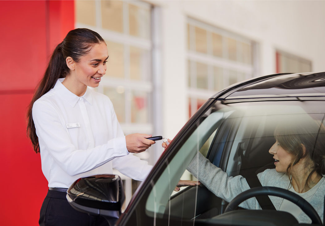 A lady handing something to a lady inside a car